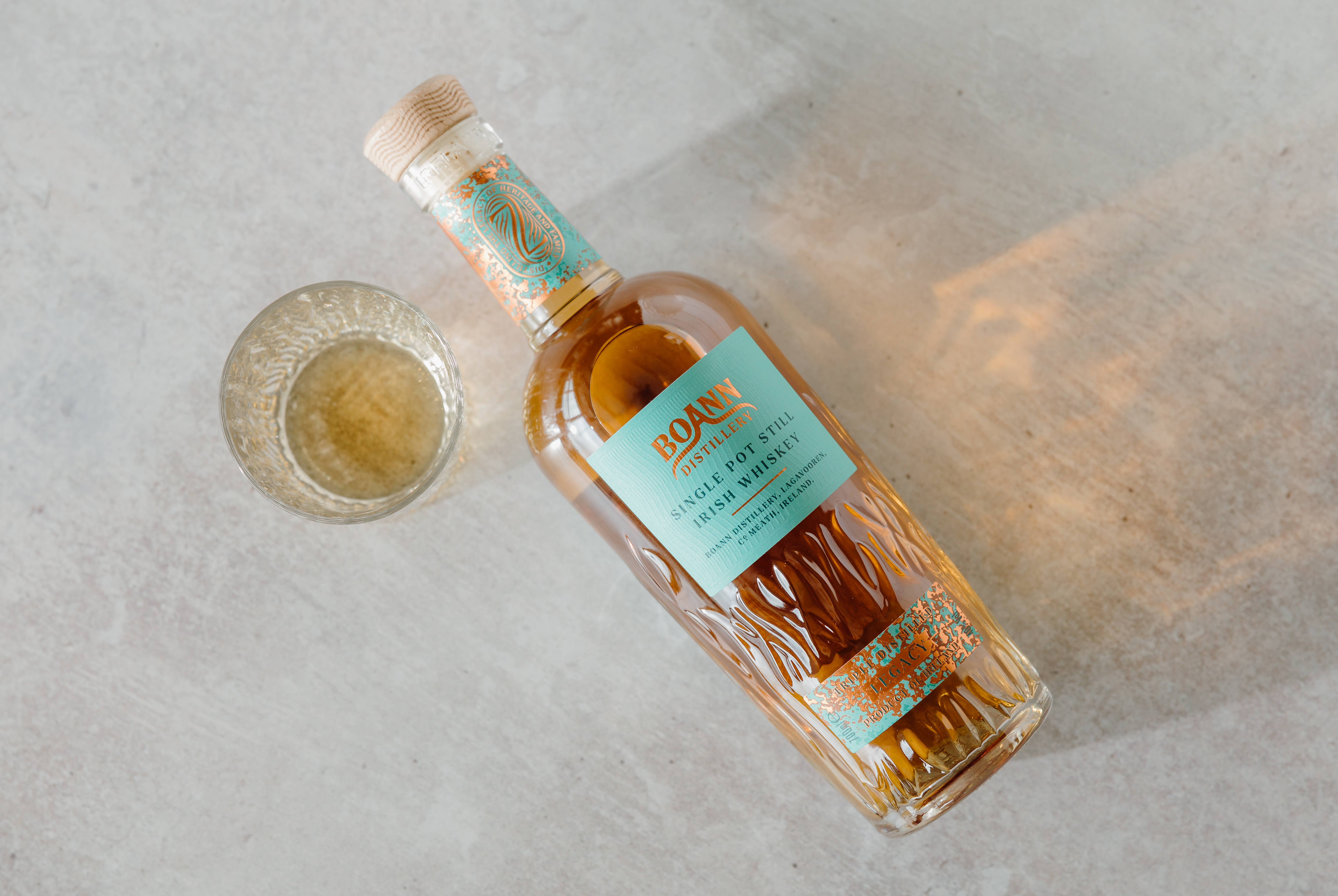 Boann Legacy Irish Whiskey with a glass, photographed on a stone surface